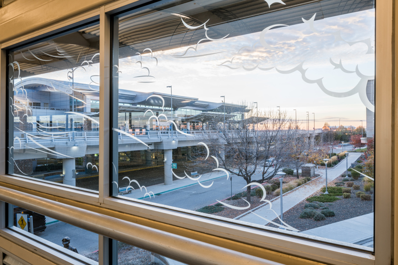 A series of windows located in the pedestrian sky bridge connecting the Boise Airport with a parking garage. On the windows are white vinyl stickers in the shapes of wisping clouds.