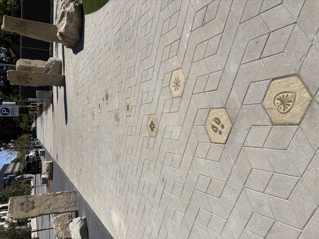An image of hexagonal sidewalk pavers with brass inlays of symbols seen in the etchings of the Ancestral Pillars.