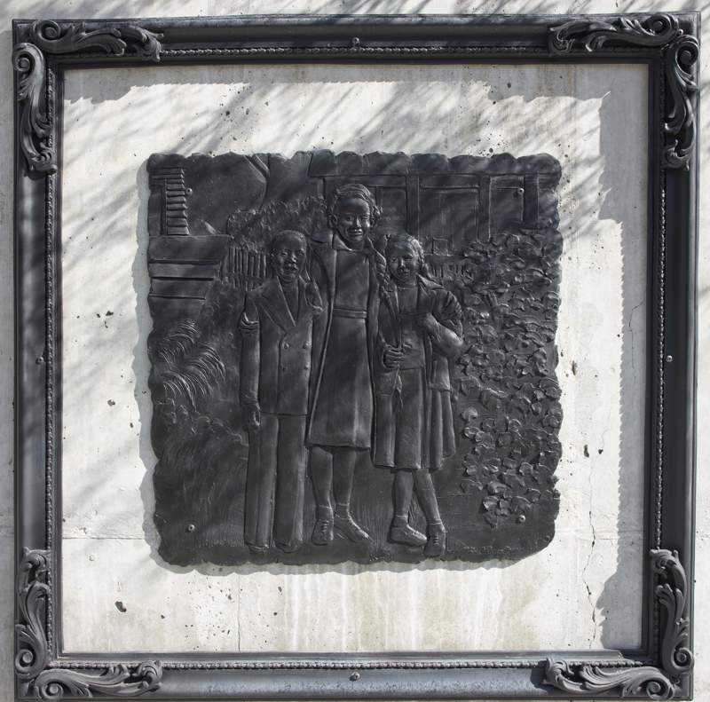 A low bas-relief bronze resin sculpture depicting a photo of 3 children. The sculpture is square with a rough edge and is surrounded by a separate ornate frame.